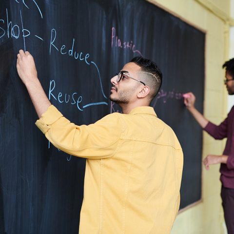 Men writing reduce, reuse, recycle on board.