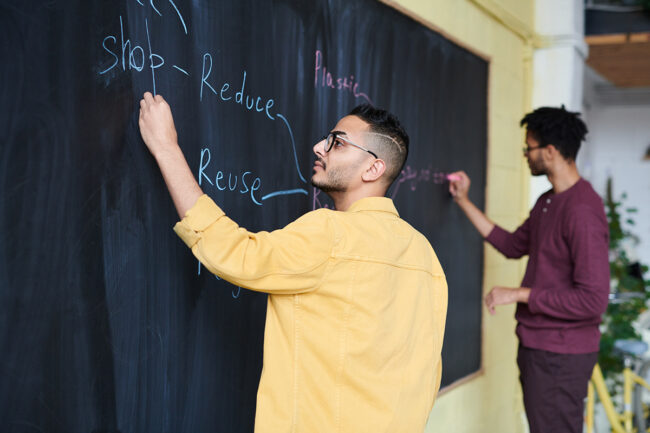 Men writing reduce, reuse, recycle on board.