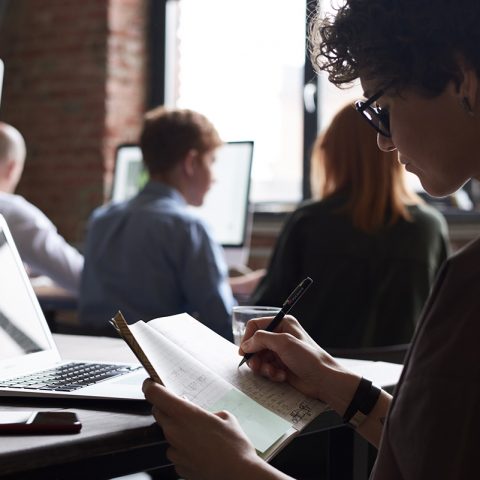 Person writing notes in a busy office.
