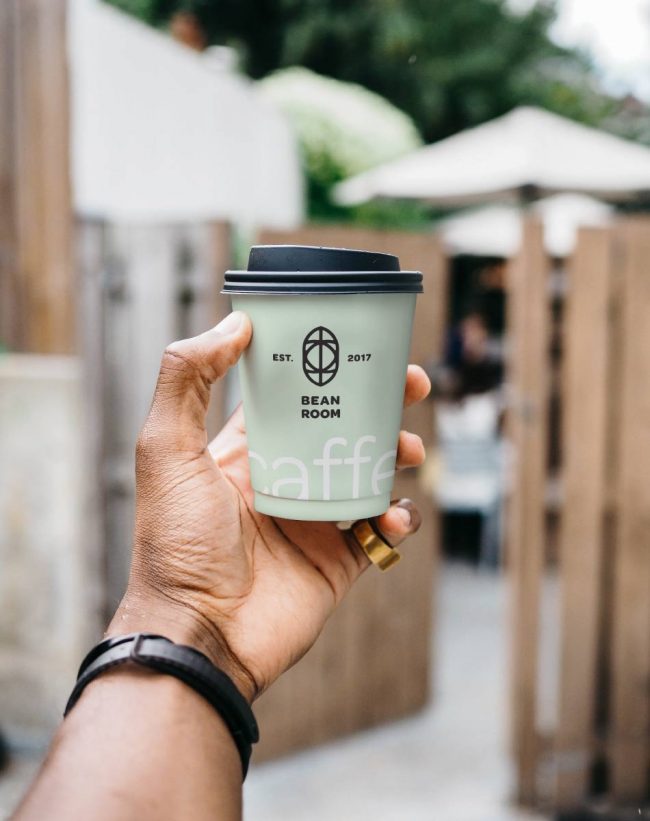 Here's an alt text option: Hand holding Bean Room coffee cup.